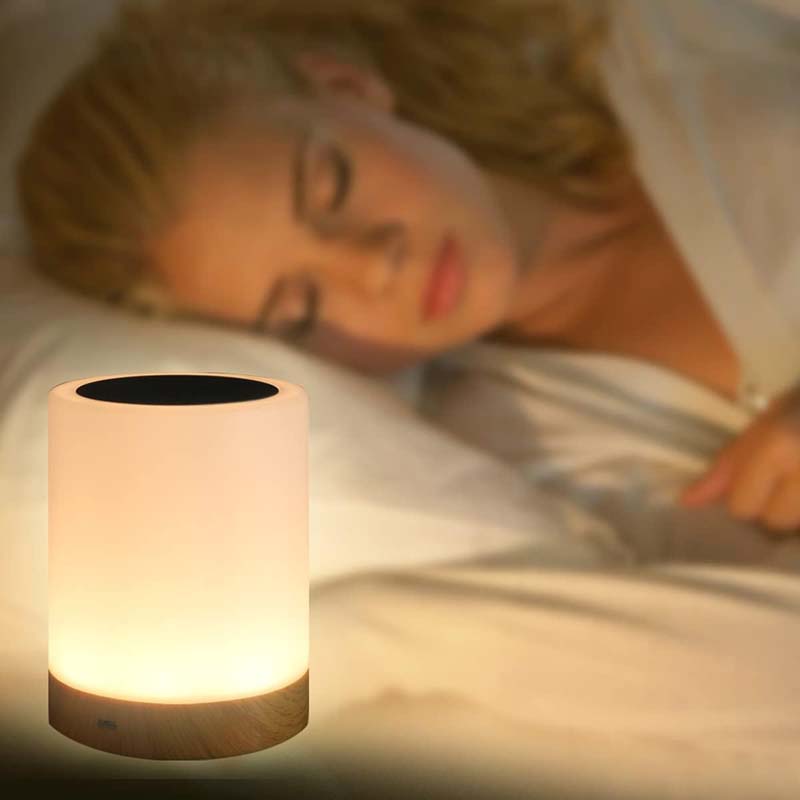 Woman lying in bed with a glowing night light on a wooden nightstand.
