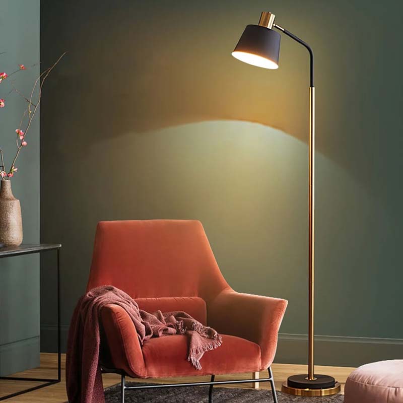 A floor lamp in a room with a green wall, an orange chair and a pink blanket on it.