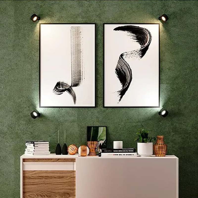 Touch Sconce around two abstract paintings on a green wall, under which decorative elements are located.