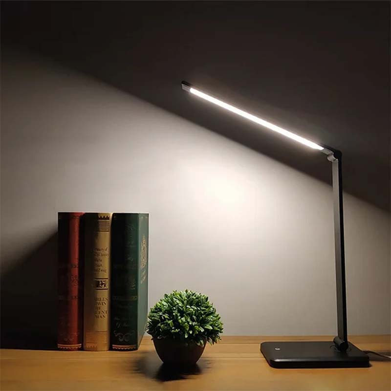 Desk lamp on a wooden surface with books and a plant in the background