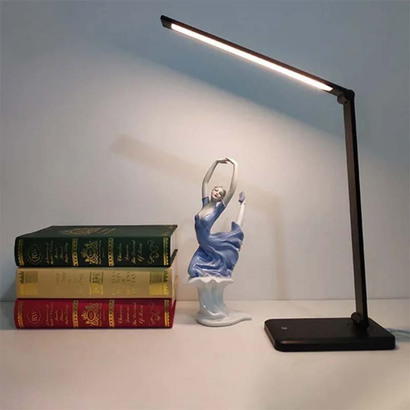 Black adjustable desk lamp on a surface with books and a figurine.