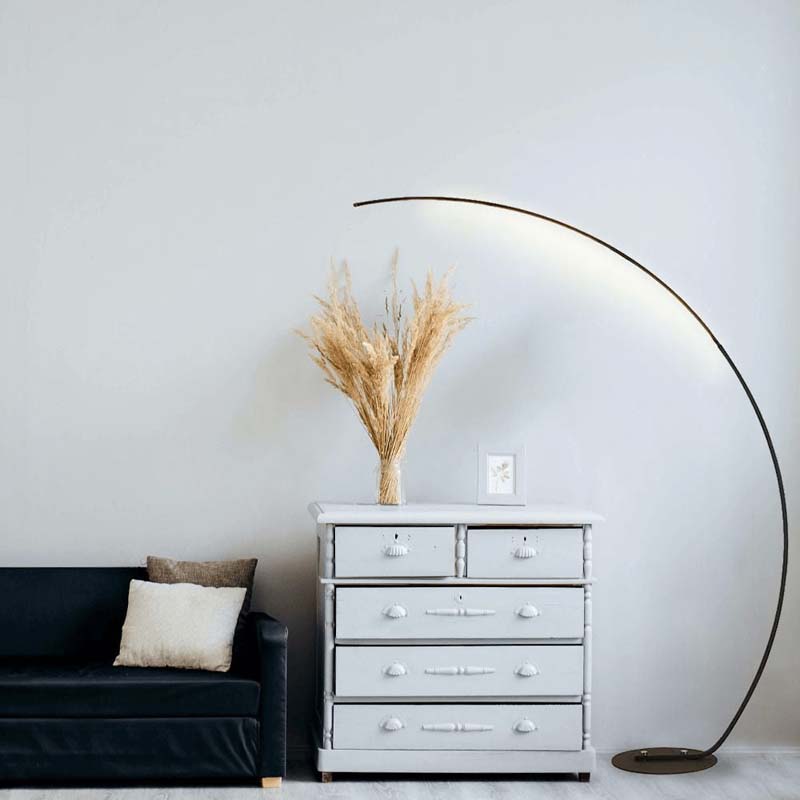 Arc floor lamp in a modern interior with a black sofa and a gray dresser