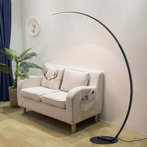 Arc floor lamp in a room with plants and blue curtains next to a light gray sofa with decorative cushions
