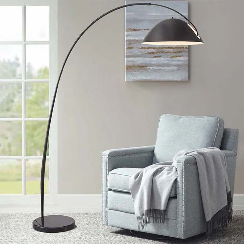 Arc floor lamp with a black shade positioned over an armchair.