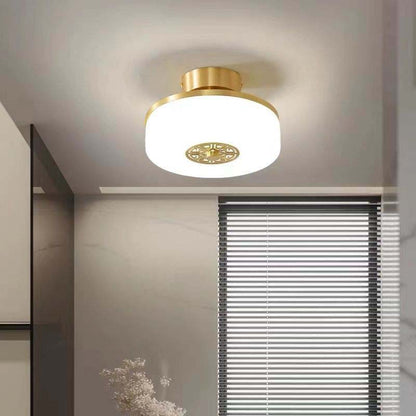 Ceiling light fixture with gold frame and white glass shade in a room setting.
