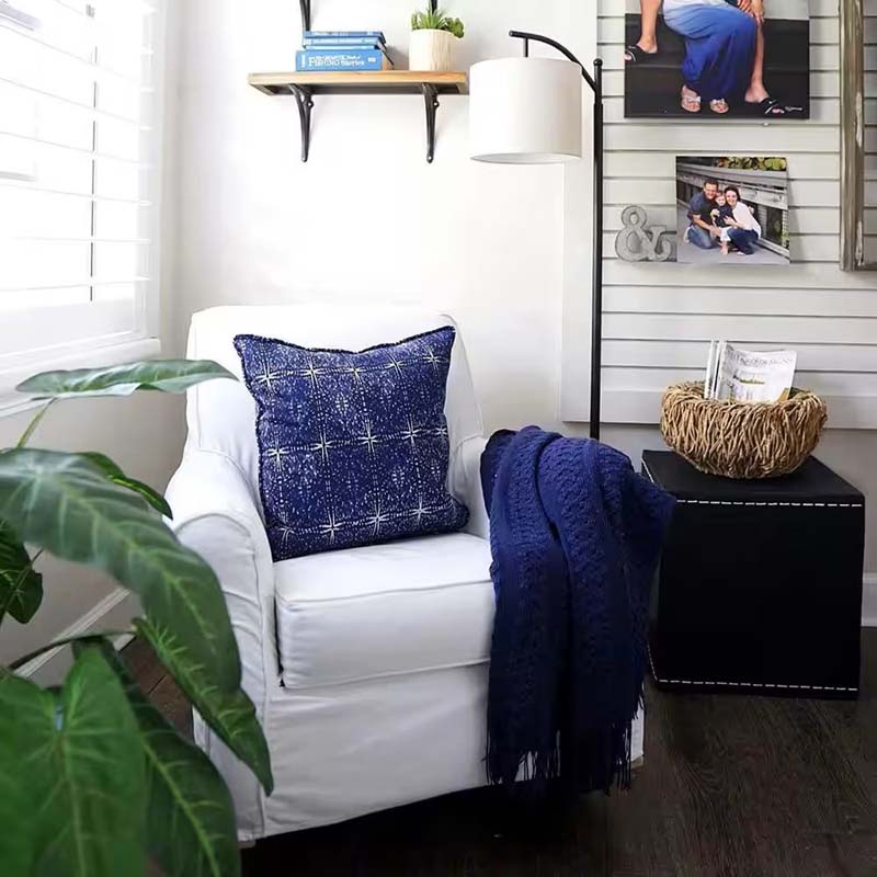 Classic black Elegant Line Floor Lamp in a cozy setting with a white armchair, blue pillow, blue throw, decorative plant, nightstand and wicker vase.