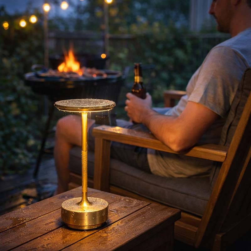 A man is sitting outdoors by a fire, a portable table lamp is burning on the table.