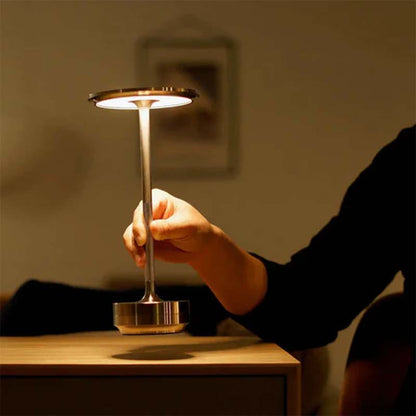 Man holding portable metal table lamp over wooden surface against blurred background.