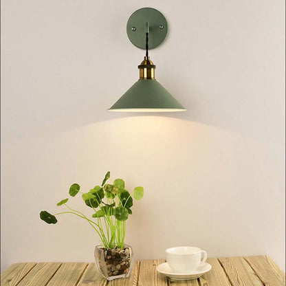 Green wall lamp on a white wall with a plant and cup on a wooden surface.