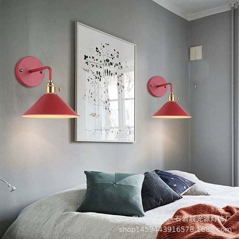 Two red wall lamps on a gray wall with a bed and pillows in the foreground.