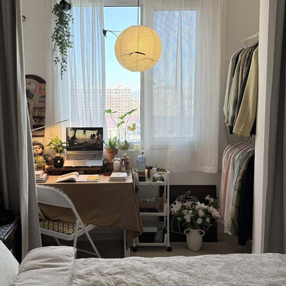 Cozy workspace by the window with a laptop, plants, and a hanging paper lamp.