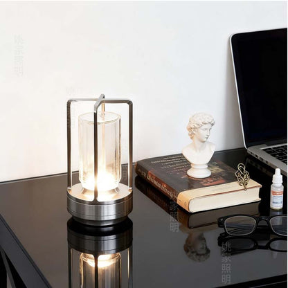 Modern desk lamp on a reflective surface with books and a laptop in the background