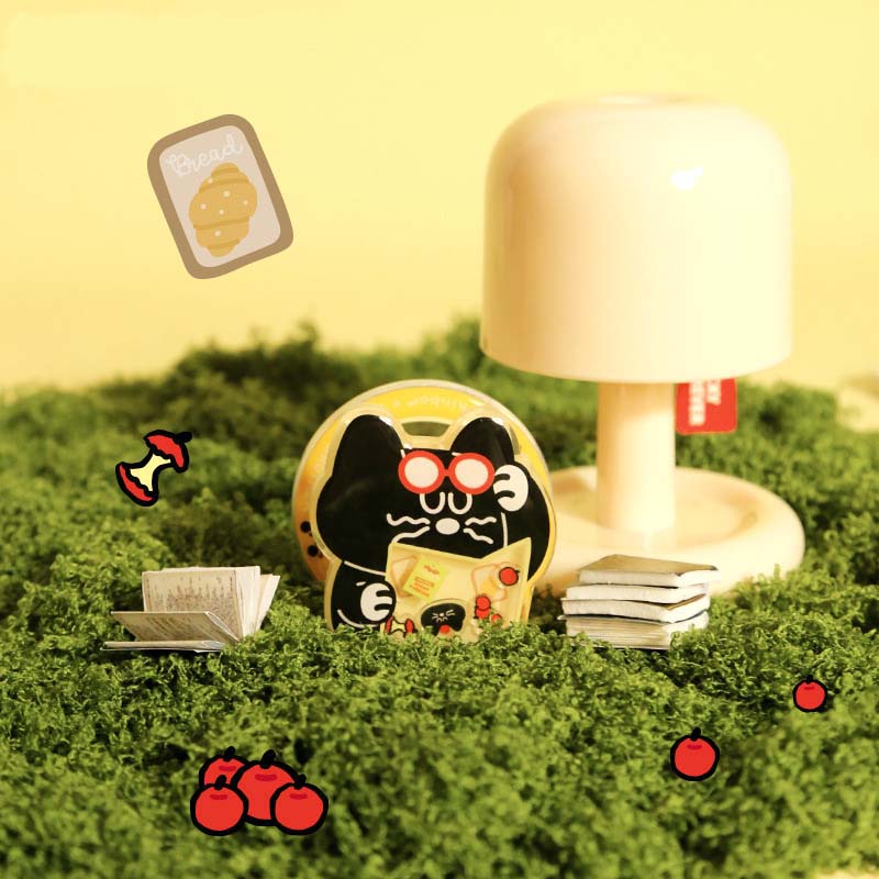 Decorative scene with a cartoon cat, books, and a lamp on a grassy surface.