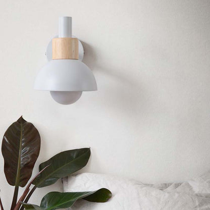 Wall-mounted light fixture with wooden accent on a white wall, next to a plant.