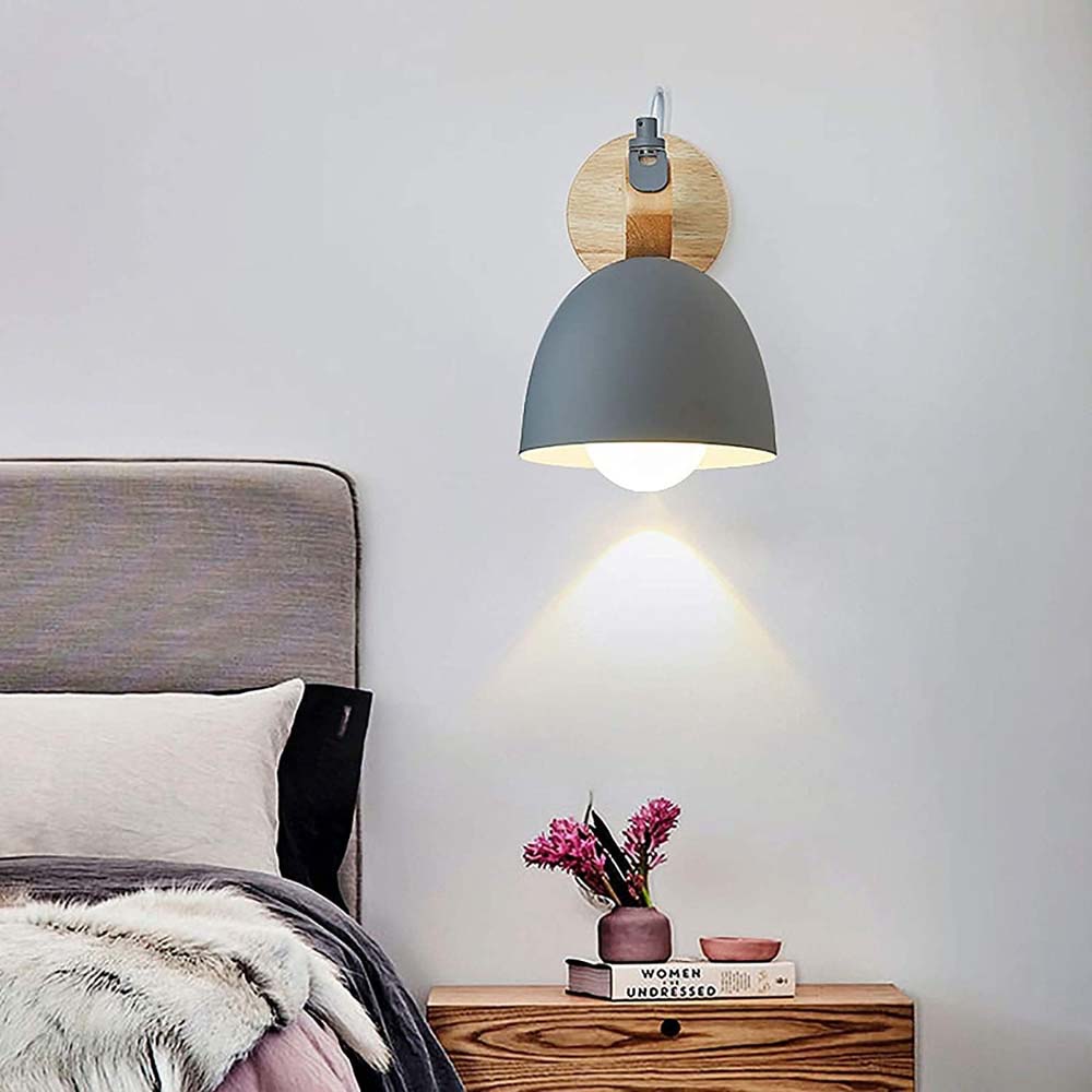 A grey wall lamp hangs on the wall above a wooden nightstand with books and a vase.