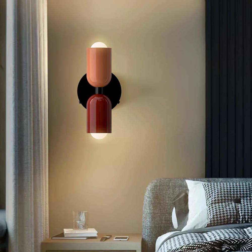 Modern wall sconce with red and orange design on a beige wall above a bed.