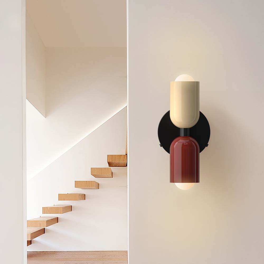 Modern wall sconce with a candle-like design on a white wall next to a staircase.