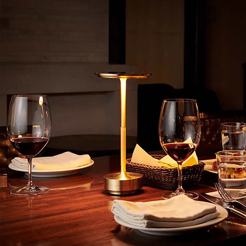 Dining table setting with wine glasses, a lamp, and plates in a dimly lit room.