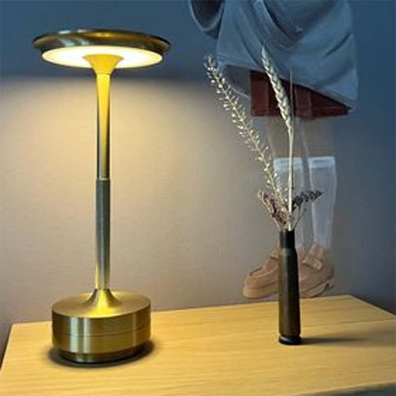 Gold lamp on a wooden surface with a vase of flowers in the background