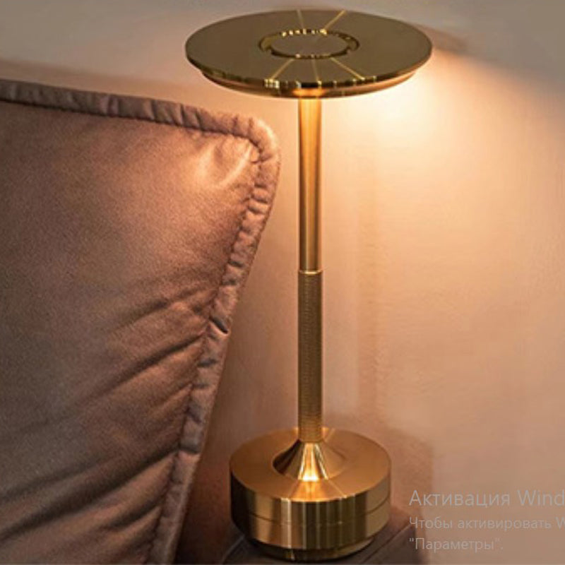 Eclipse Wireless Touch LED Lamp Gold on the bedside table next to the bed with soft focus background