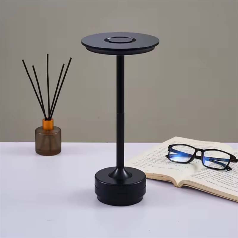 Black table lamp on white surface, book and glasses in the background.