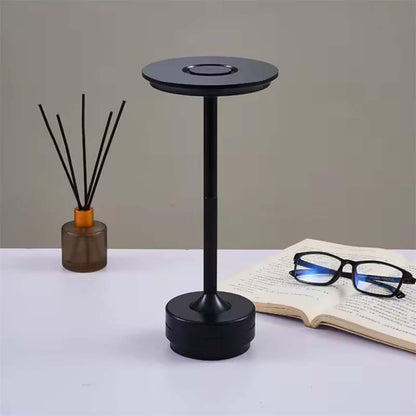 Black table lamp on white surface, book and glasses in the background.