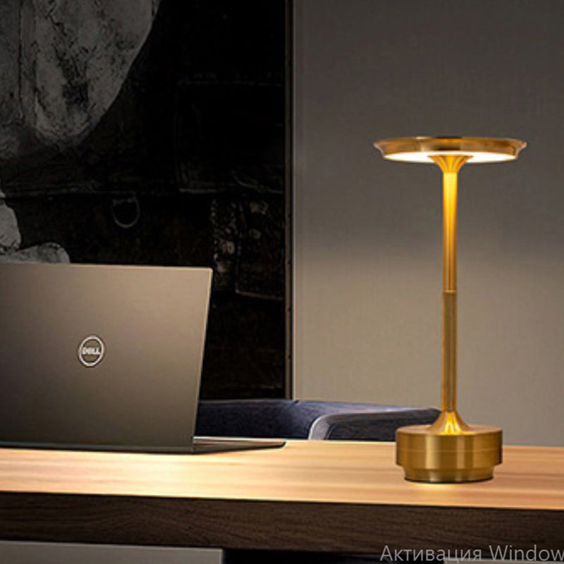 Gold desk lamp on a wooden surface next to a laptop with a dark background