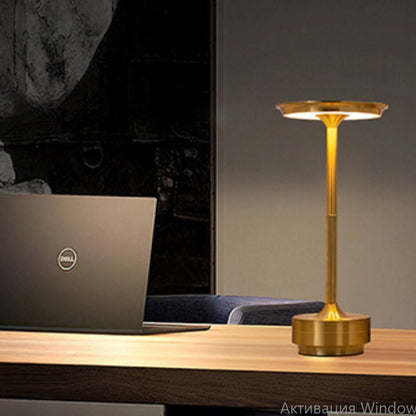 Gold desk lamp on a wooden surface next to a laptop with a dark background