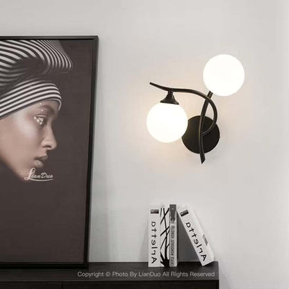 Modern wall sconce with two round lights on a white wall, next to a framed portrait and books.
