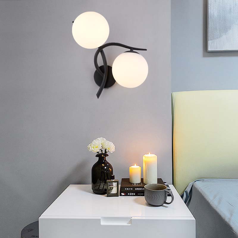 Modern wall sconce with two round lights on a gray wall above a white nightstand with decorative items.