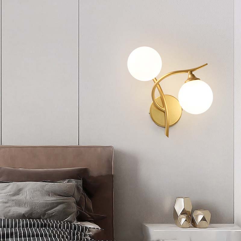 Gold wall sconce with two round lights on a neutral wall above a bed.