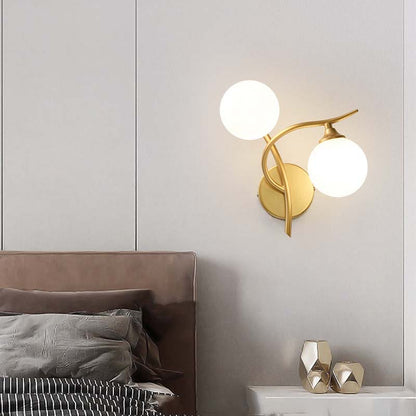 Gold wall sconce with two round lights on a neutral wall above a bed.