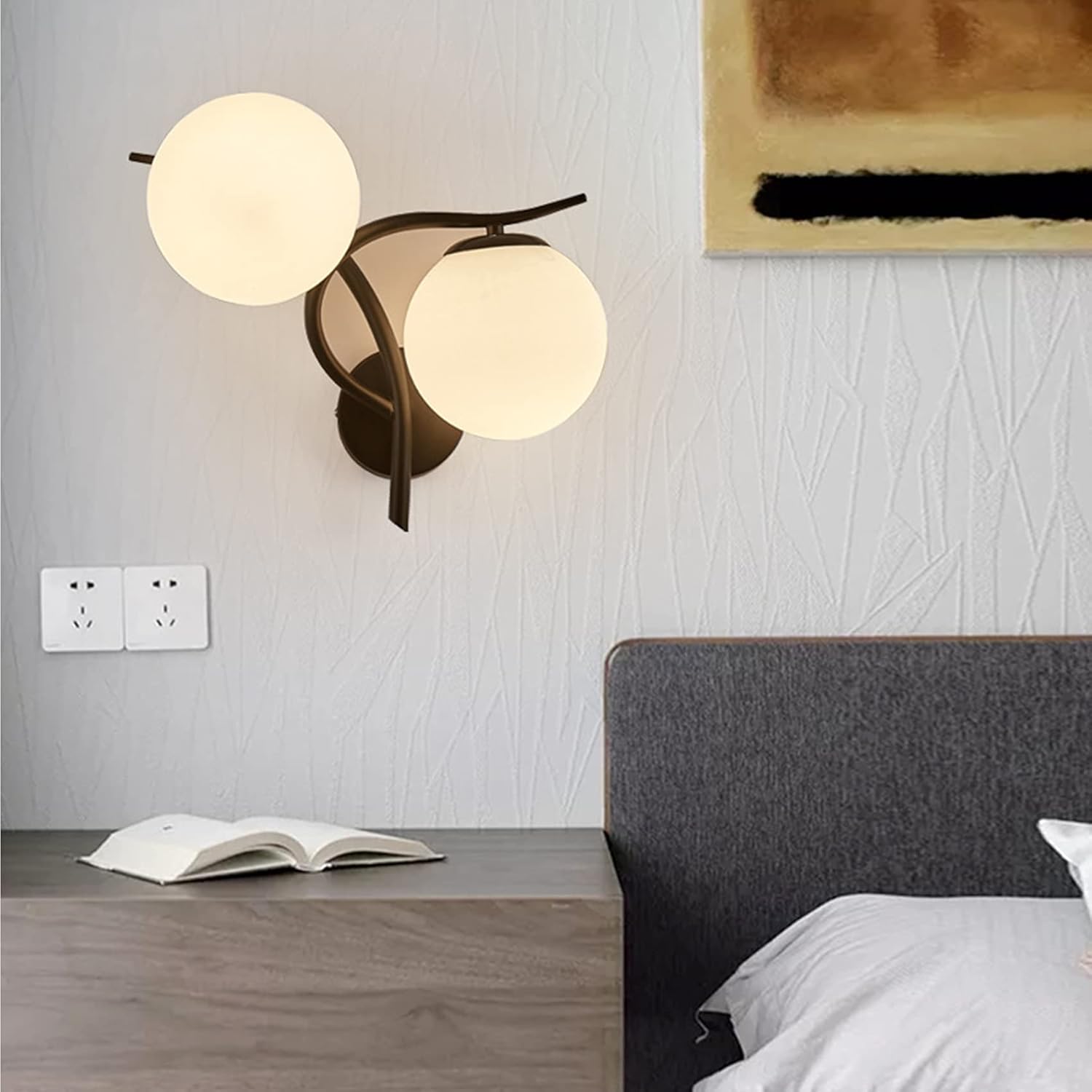 Modern wall lamp with two round lights on a gray wall above a bed.
