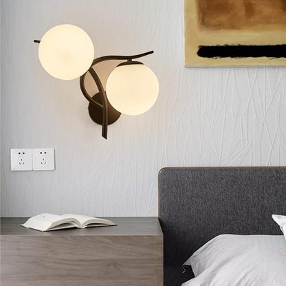 Modern wall lamp with two round lights on a gray wall above a bed.
