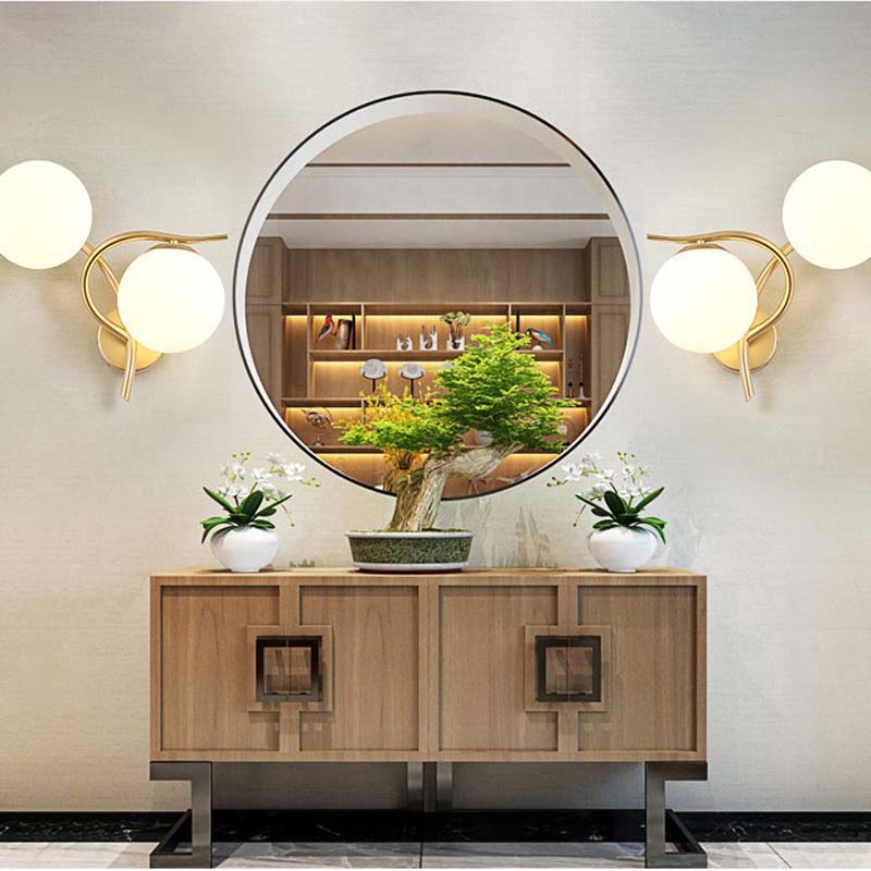 Round mirror above a wooden console table with wall lights and plants in a room.