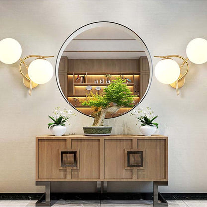 Round mirror above a wooden console table with wall lights and plants in a room.