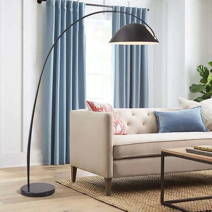 Floor lamp Bowl, black arched design with a hemispherical shade in a living room above a sofa.