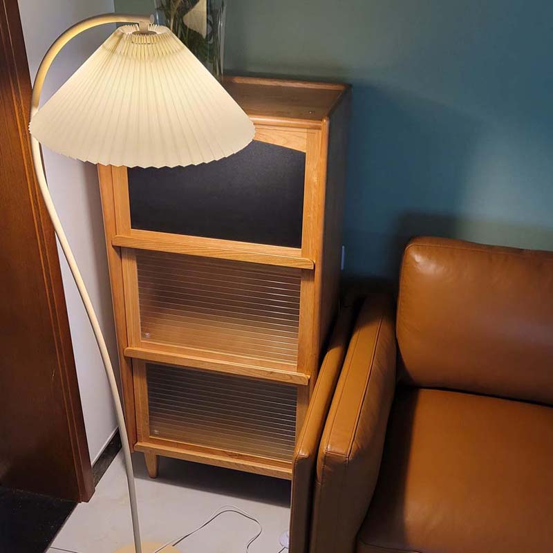 Floor lamp with pleated shade next to a wooden cabinet
