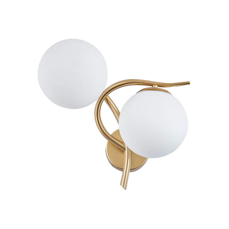 Wall-mounted light fixture with two white spherical shades and gold metal arm on a white background
