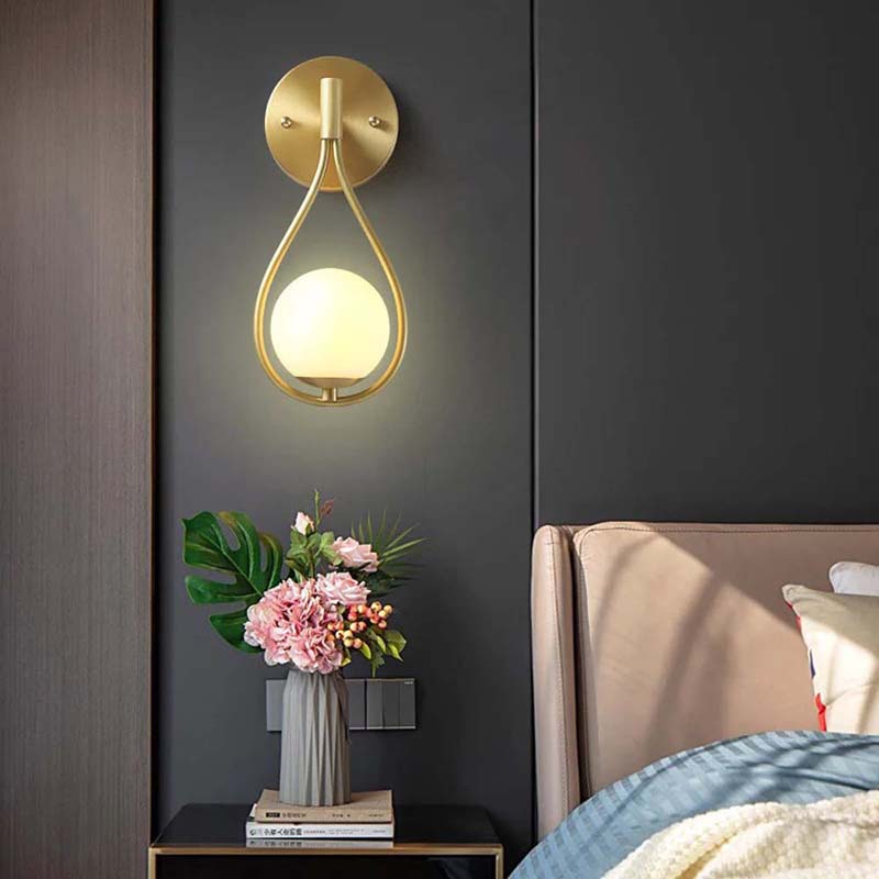 Gold wall sconce on a dark wall with a vase of flowers and books on a nightstand.