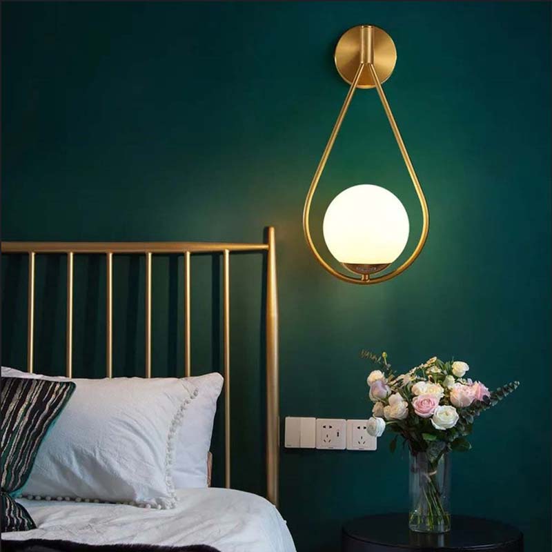 Gold wall sconce with a white bulb on a green wall above a bed.