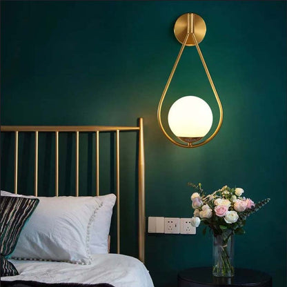 Gold wall sconce with a white bulb on a green wall above a bed.