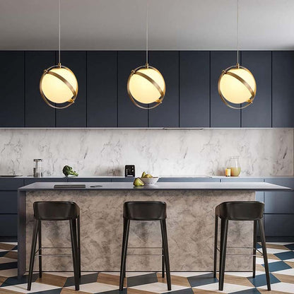 A golden framed globe pendant with gold trim in a
modern kitchen with a marble island and bar stools.