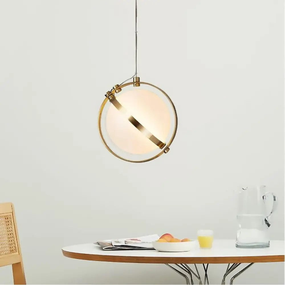 A golden framed globe pendant with gold trim hangs over a dining table against a minimalist backdrop.