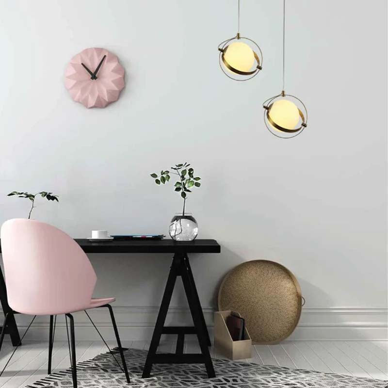 A golden framed globe pendant with gold trim is featured in a contemporary setting with a pink chair, black table and accents.