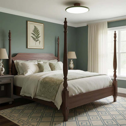 Ceiling light in a bedroom interior with a wooden canopy bed, green walls and framed paintings.