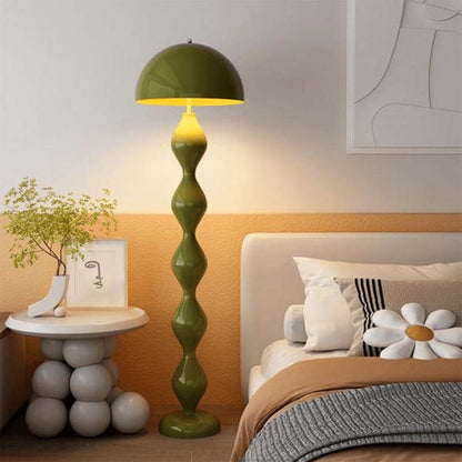 Green floor lamp in a bedroom setting with a bed and side table.