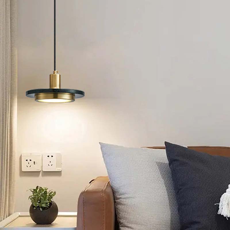 Modern pendant light fixture in a living room setting with pillows and a plant.