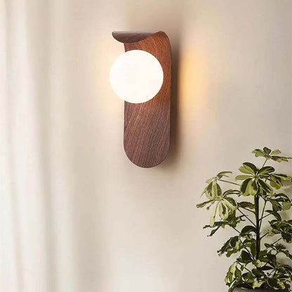 A wall lamp with a round bulb on a neutral wall, with a plant placed in the corner.