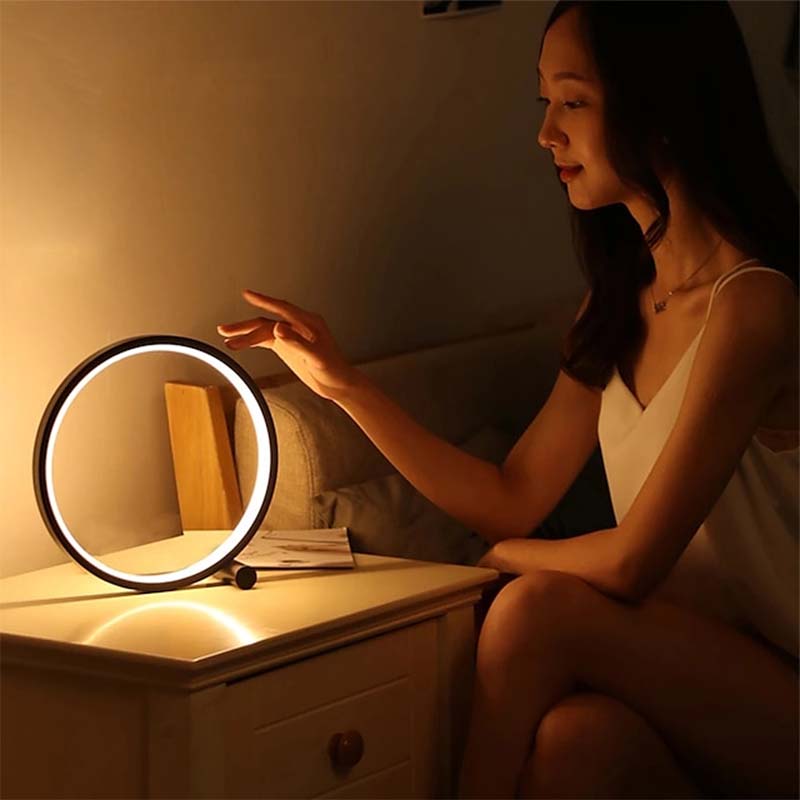 Woman using a round LED light on a nightstand in a dimly lit room.